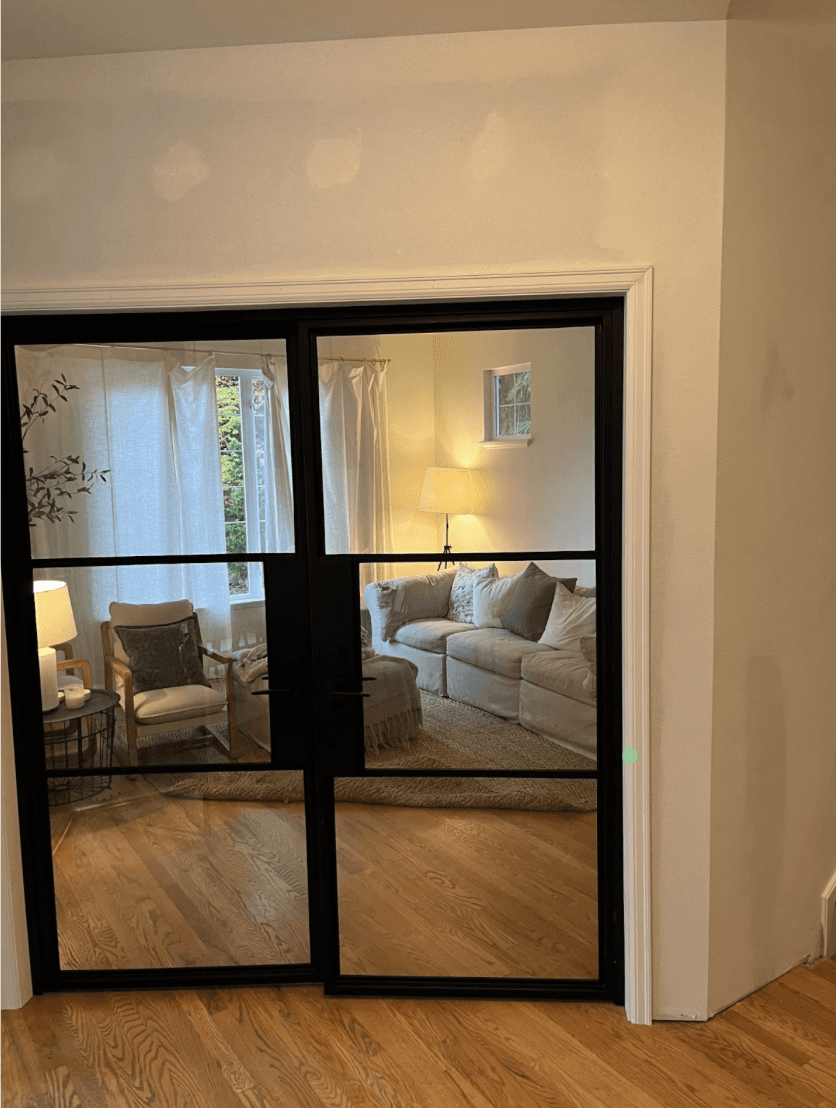 Black-framed interior French doors installed between a hallway and a living room