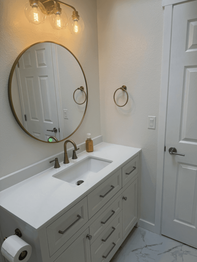 Finished bathroom remodel with a white shaker vanity, round brass mirror and Edison sconce lighting